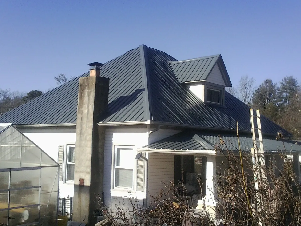 Dark blue standing seam metal roof on a white farmhouse with dormer — Slate & Tile Roof Repair by Roofing Brothers in Lawrenceville