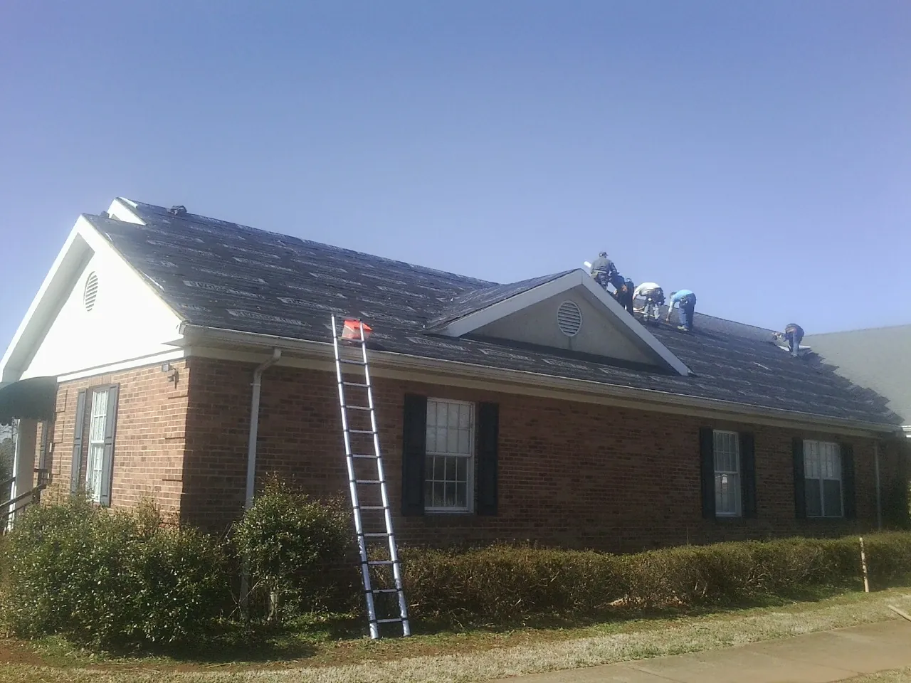 Crew tearing shingles off a brick ranch roof with a ladder set — Metal Roof Repair work by our crew in Lawrenceville